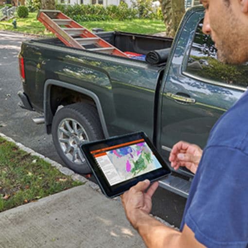 Contractor on tablet using GAF WeatherHub near truck with ladder
