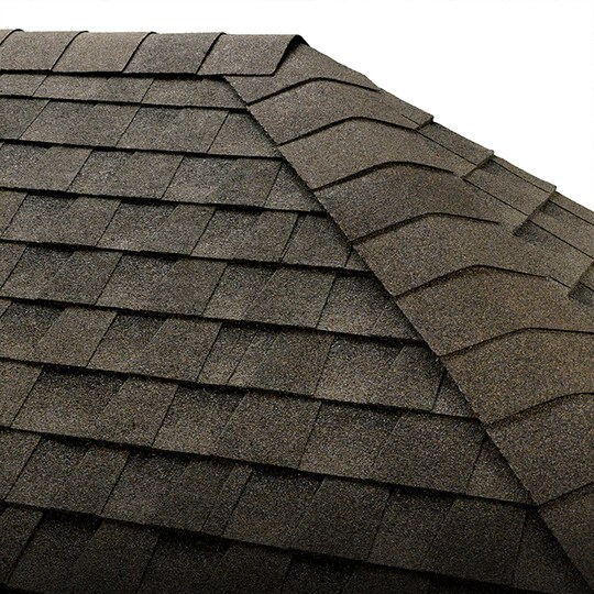 Shaded image of a GAF roofer installing GAF hip and ridge cap shingles to a residential roof