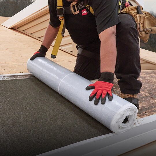 Shaded image of a GAF roofer installing GAF leak barrier on a residential roof