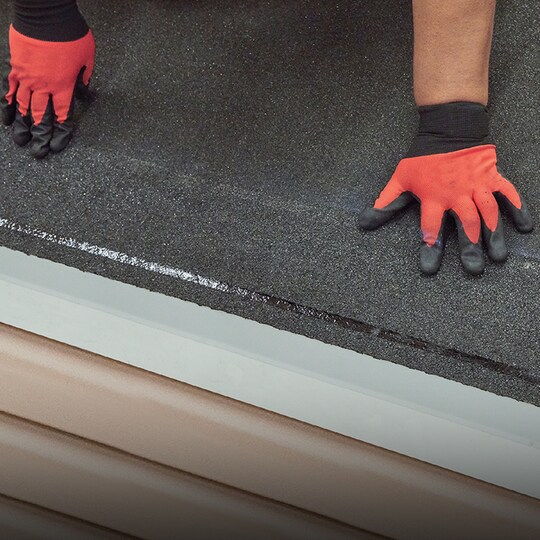 Shaded image of a roofer with white gloves installing GAF roofer strip shingles to prevent shingle blow-off