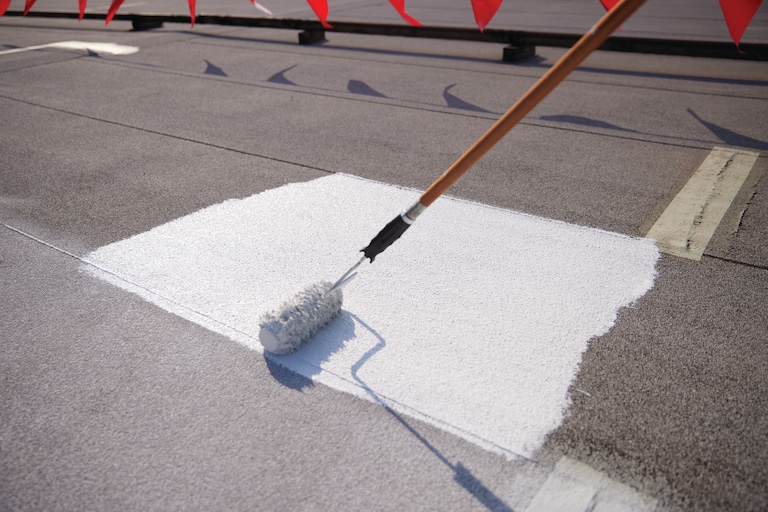 A contractor on flat roof applying GAF Multi-purpose Primer with a roller.