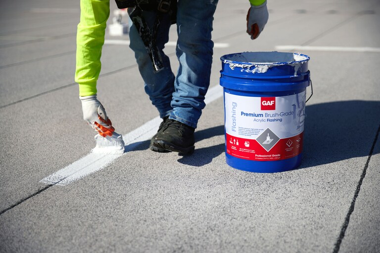 A contractor treating a seam on a flat roof with GAF Premium Brush-Grade Acrylic flashing