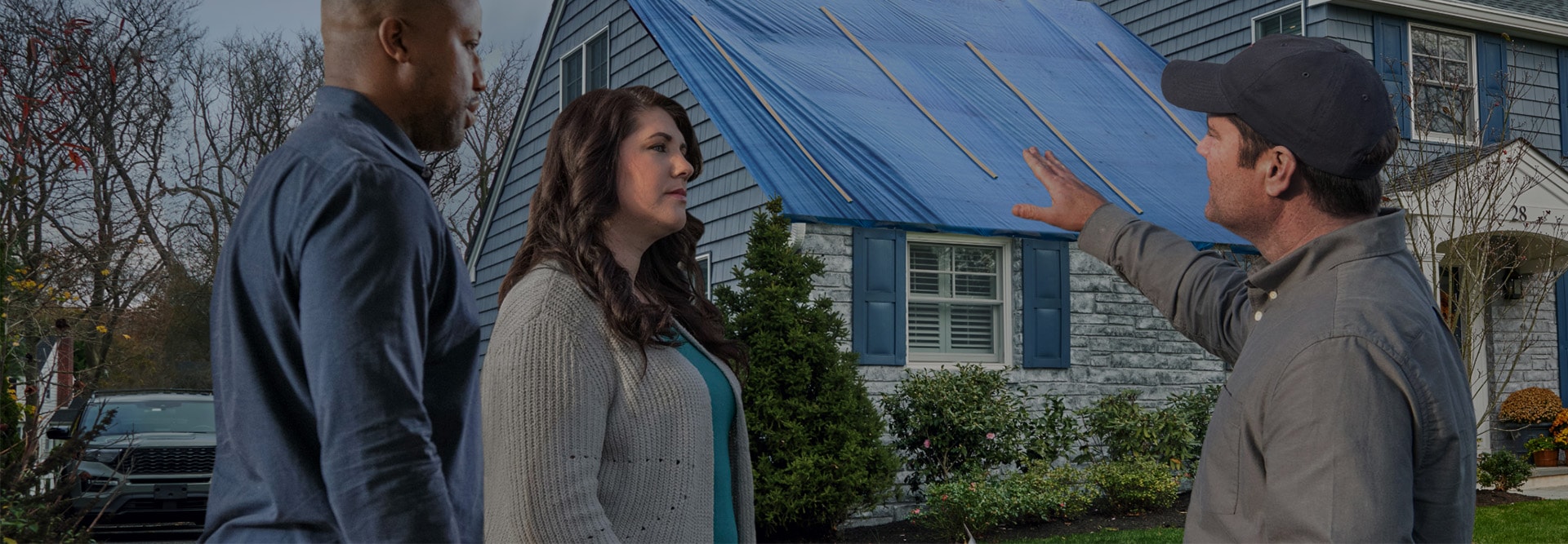 Homeowners outside house with insurance restoration contractor pointing at blue tarp on roof