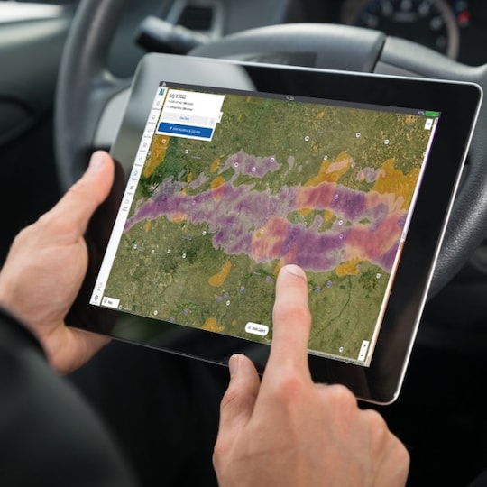 Hands holding tablet in vehicle with GAF WeatherHub on screen