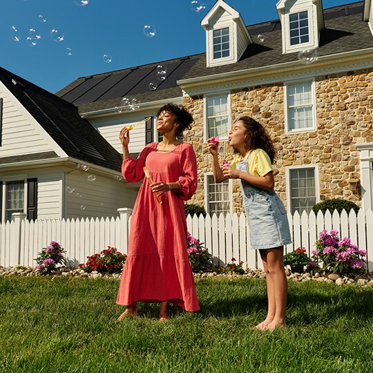 Mother and daughter blowing bubbles outside home with a solar roof