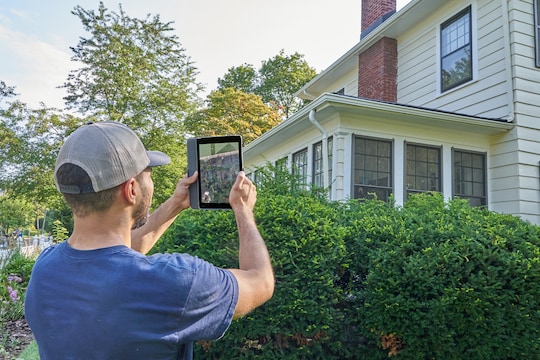 Roofing contractor holding tablet up in front of home to review roof documents