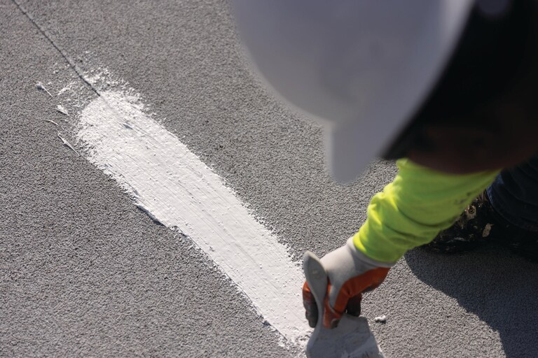 A contractor treating a seam on a flat roof with GAF Silicone Mastic